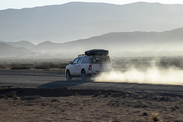 4x4 por pista de Namibia al atardecer y su estela blanca del polvo de la pista 